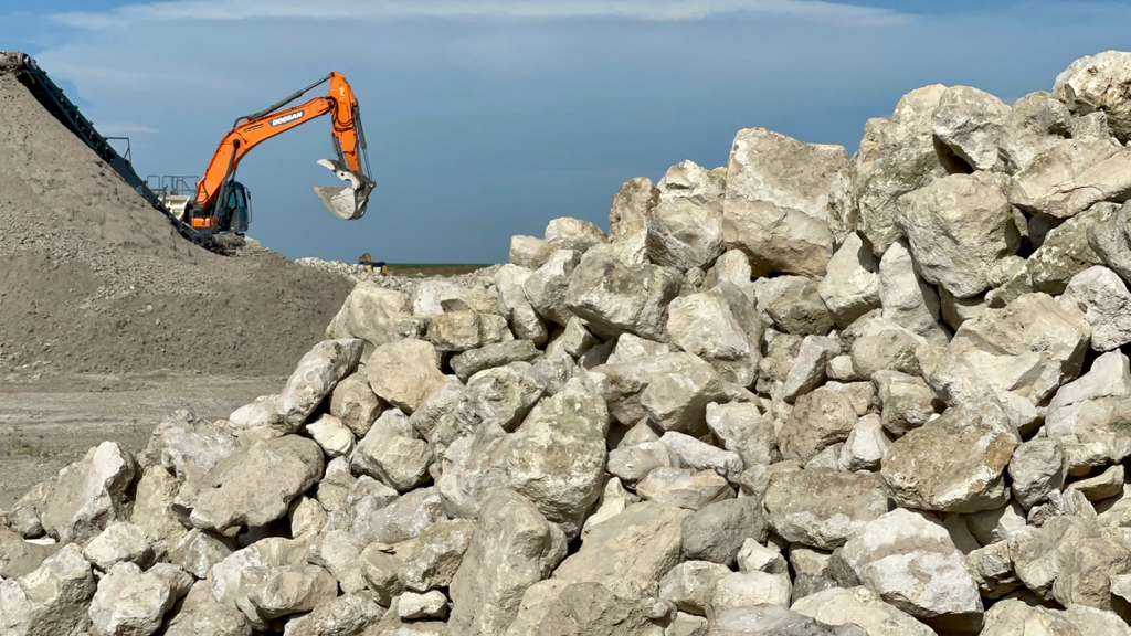 Excavator placing riprap rocks for shoreline erosion control in Florida